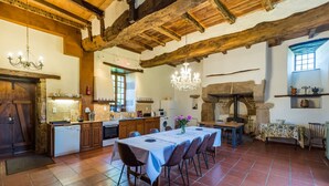 A rustic kitchen with wooden beams, a dining table set for six, and a stone fireplace. - Le Manoir - Plouguiel (Plouguiel)