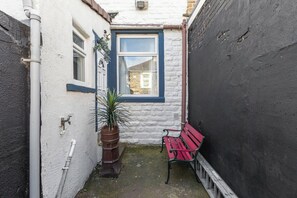 A narrow courtyard with a red bench, a window with a blue frame, and a potted plant. - Spacious 3BR Home Near Burnley Town Centre (Lancashire)
