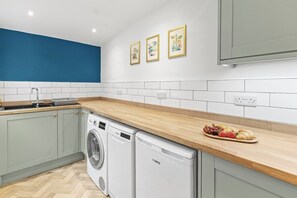 A kitchen with a washing machine, a sink, and a countertop with fruits. - Spacious 3BR Home Near Burnley Town Centre (Lancashire)