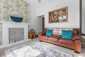 Ein Wohnzimmer mit Kamin, einer braunen Ledersofa, einem gemusterten Teppich und einem gerahmten Gemälde an der Wand.