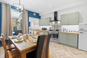A modern kitchen with a dining area, featuring a wooden table, chairs, and a built-in oven. - Spacious 3BR Home Near Burnley Town Centre (Lancashire)