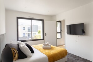 A modern hotel room with a large bed, a flat-screen TV, and a window with a view of buildings outside. - La Villa Meunier - Four Bedroom House, Sleeps 7 (Dinard)