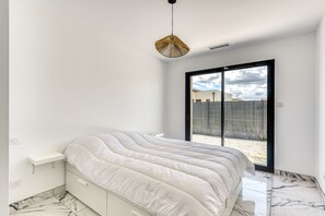 A bedroom with a bed, a hanging light fixture, a sliding glass door, and a white wall. - L'Instant Minervois - Avec piscine privée (Olonzac)