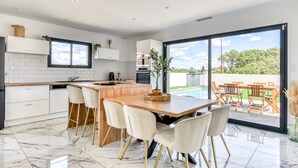 A modern kitchen with a large island, white cabinetry, and a view of a swimming pool. - L'Instant Minervois - Avec piscine privée (Olonzac)