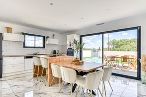 A modern kitchen with a large island, white cabinetry, and a view of a swimming pool. - L'Instant Minervois - Avec piscine privée (Olonzac)