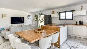 A modern kitchen with white cabinetry, a wooden dining table, and a built-in island. - L'Instant Minervois - Avec piscine privée (Olonzac)