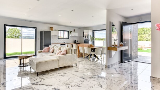A spacious living area with a sofa, dining table, and chairs, a kitchen with modern appliances, and large sliding glass doors to a patio. - L'Instant Minervois - Avec piscine privée (Olonzac)