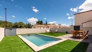 A rectangular swimming pool with a tiled deck, surrounded by well-maintained grass, a wooden table with chairs, and a shed. - L'Instant Minervois - Avec piscine privée (Olonzac)