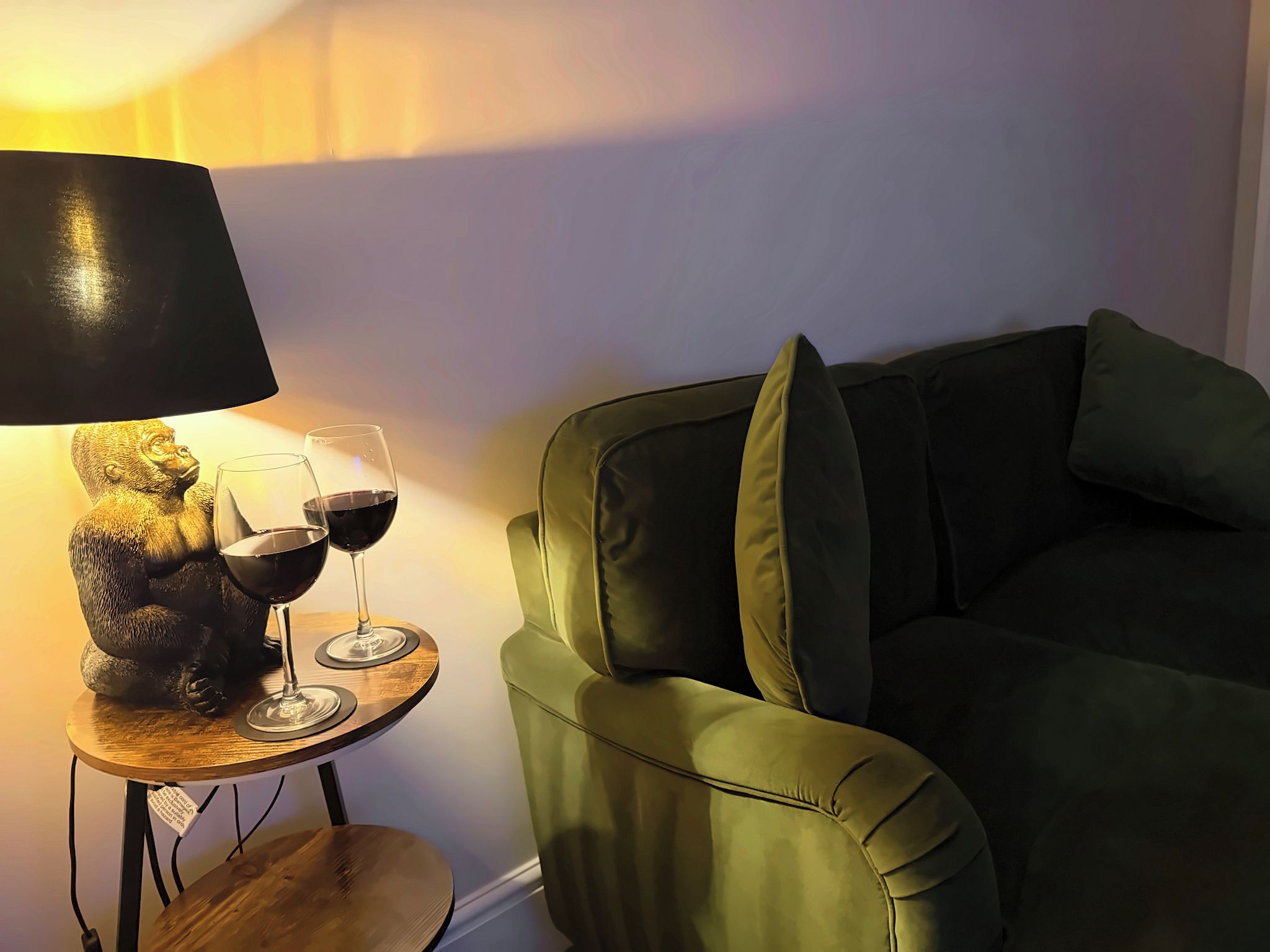 A green sofa with cushions, a small wooden table with a lamp and two wine glasses.