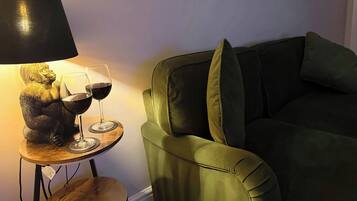 A green sofa with cushions, a small wooden table with a lamp and two wine glasses.
