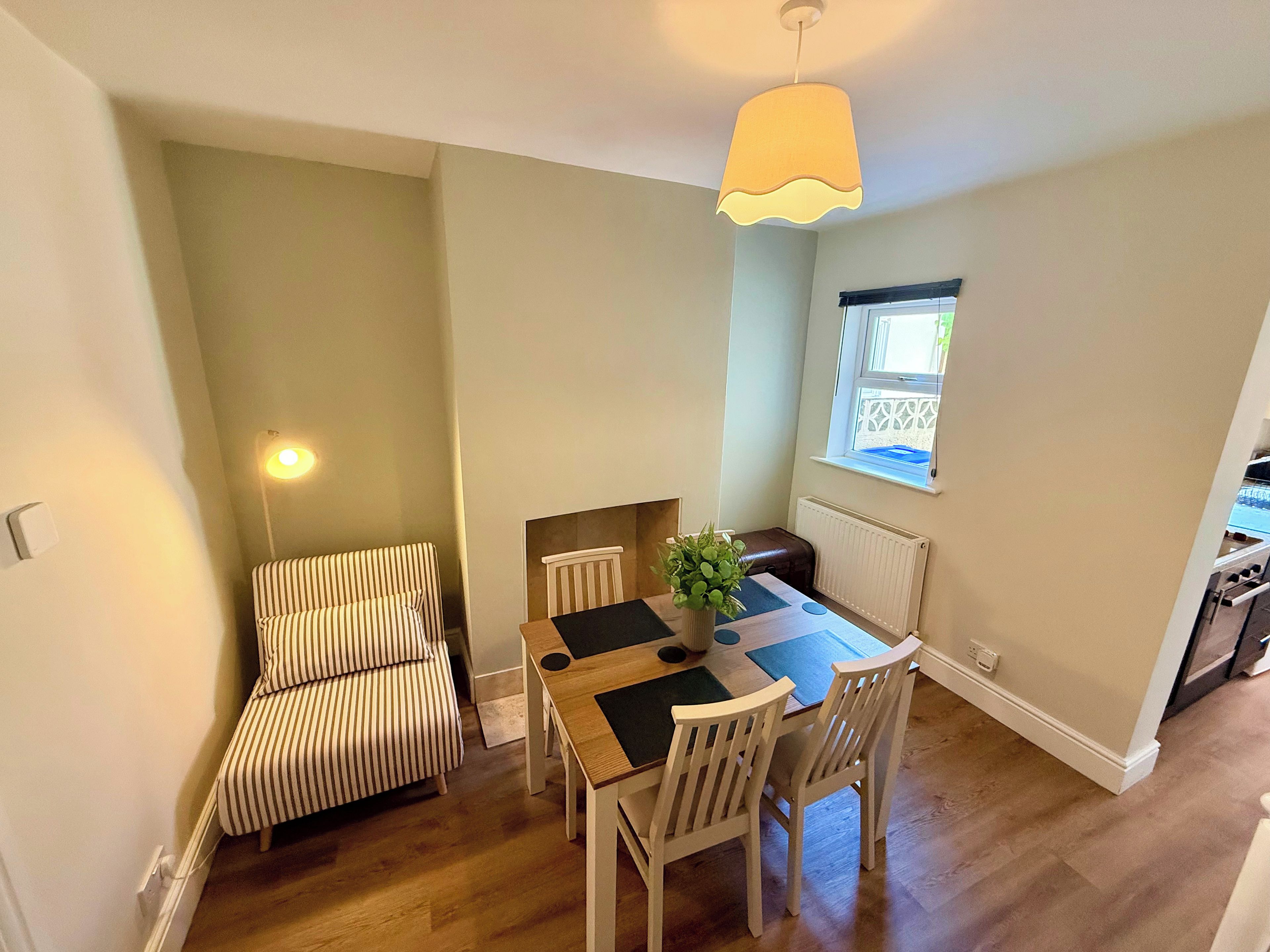 A dining area with a table, chairs, a striped sofa, a hanging light fixture, and a window with a view.