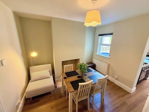 A dining area with a table, chairs, a striped sofa, a hanging light fixture, and a window with a view.