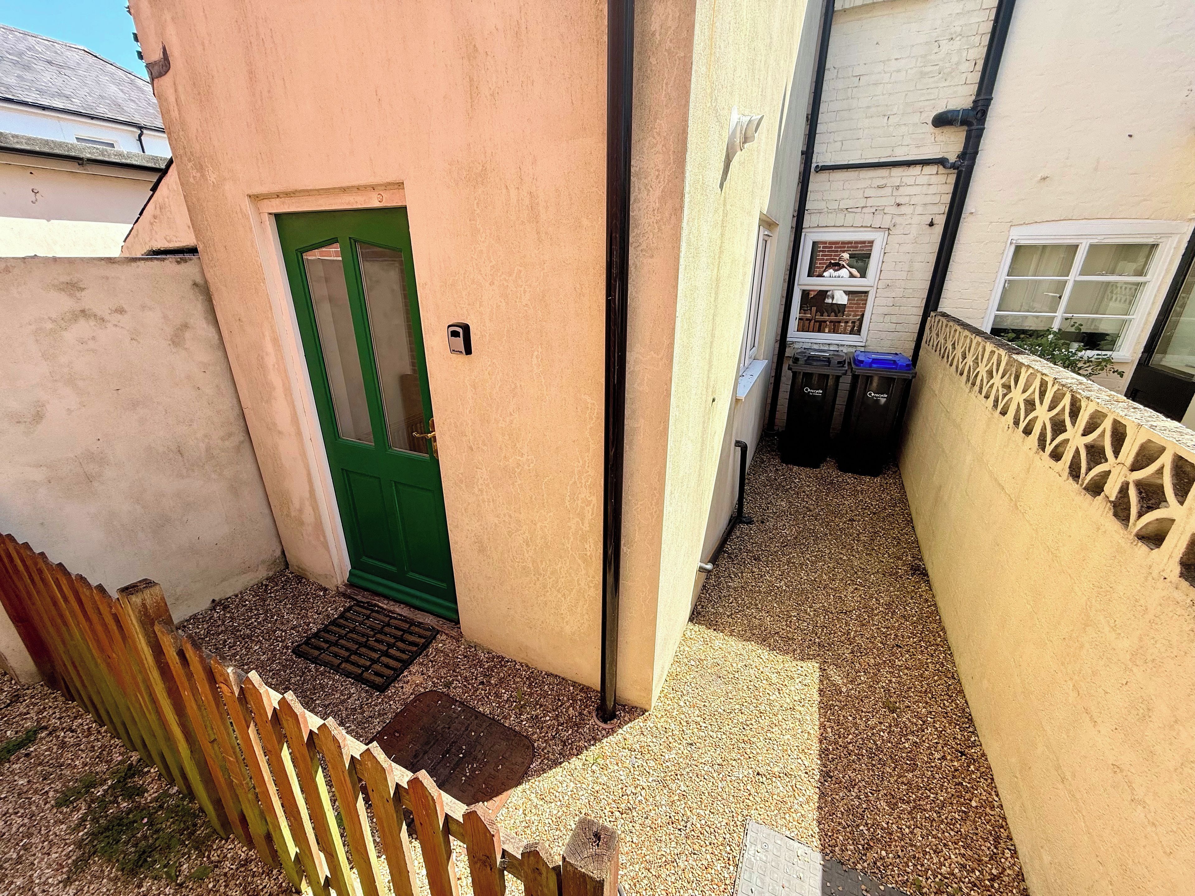 A narrow alleyway with a green door, a wooden fence, and a wall with a decorative pattern.