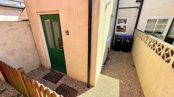 A narrow alleyway with a green door, a wooden fence, and a wall with a decorative pattern.