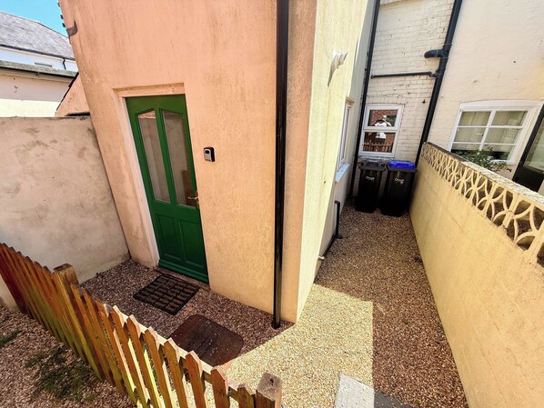 A narrow alleyway with a green door, a wooden fence, and a wall with a decorative pattern.
