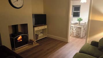 A living room with a fireplace, a television on a stand, and a dining area visible through an open door.