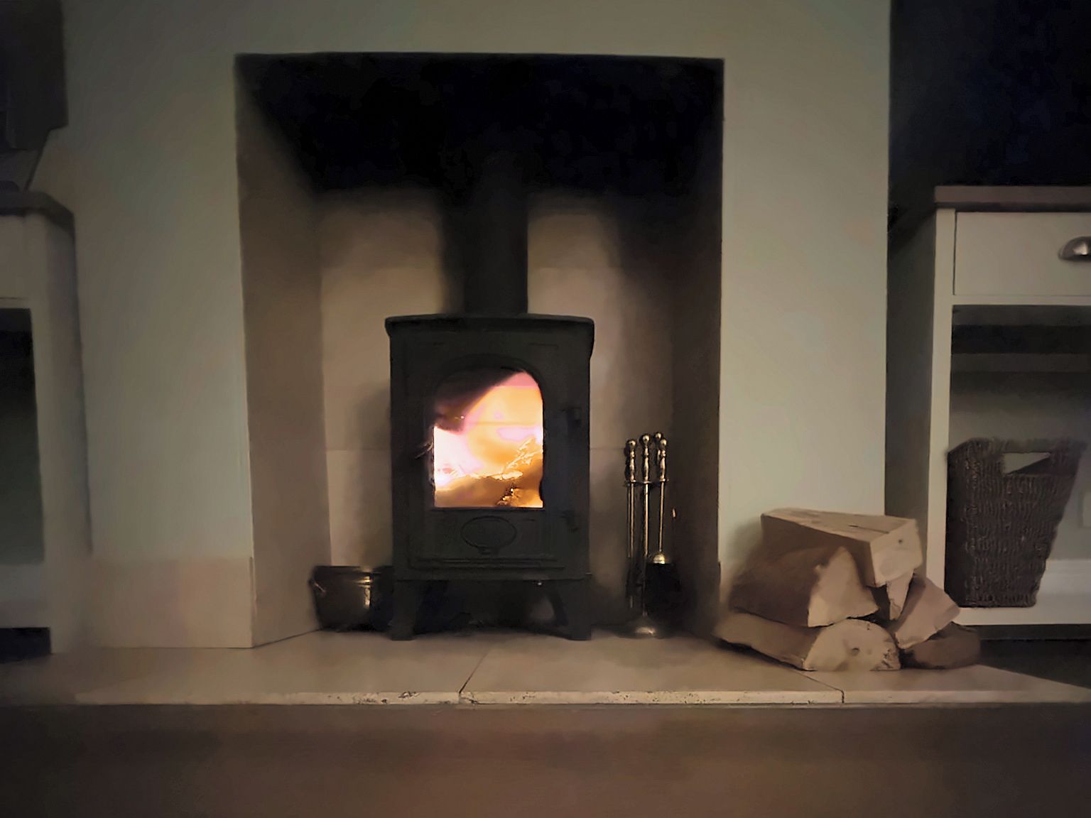 A wood-burning stove with a visible fire, a small trash bin, and a wicker basket on the floor.