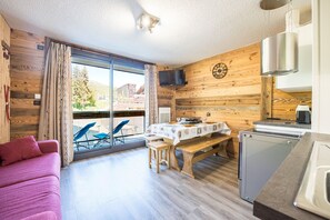 Ein Zimmer mit Holzeinrichtung, einem Esstisch mit Stühlen, einem Sofa, einem Fernseher und einem Fenster mit Vorhängen.