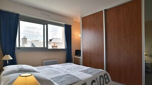 Hotellihuone, jossa on sänky, ikkuna verhoilla, lamppu, televisio ja vaatekaappi.