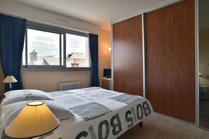 A hotel room with a bed, a window with curtains, a lamp, a TV, and a wardrobe. - L'Échappée Dinardaise - À 400 m de la plage (Dinard)