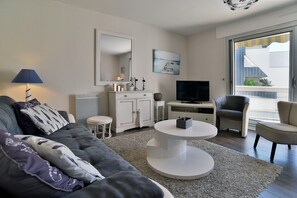 A modern living room with a sofa, a coffee table, a TV, and a balcony view. - L'Échappée Dinardaise - À 400 m de la plage (Dinard)