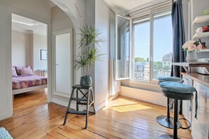 A room with a bed, a stool, a window, and a view of buildings. - Les Toits Lumineux de Vincennes - Proche château (Vincennes)