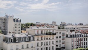 Paesaggio urbano con diversi edifici, tra cui un edificio bianco in evidenza con un balcone e un edificio grigio con tetto spiovente.