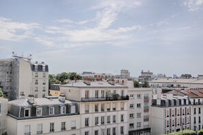 A cityscape with multiple buildings, including a prominent white building with a balcony and a grey building with a sloped roof. - Les Toits Lumineux de Vincennes - Proche château (Vincennes)