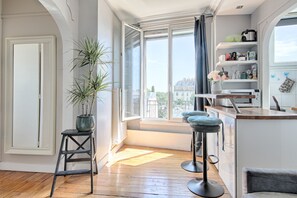 A modern kitchen with a large window, wooden flooring, and a bar area with stools. - Les Toits Lumineux de Vincennes - Proche château (Vincennes)