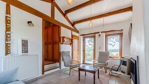 A spacious living room with wooden beams, a fireplace, a television, and a view of the outdoors. - La Chaumière de Jeannot - Maison avec jardin pour 8 (La Chapelle-Hermier)