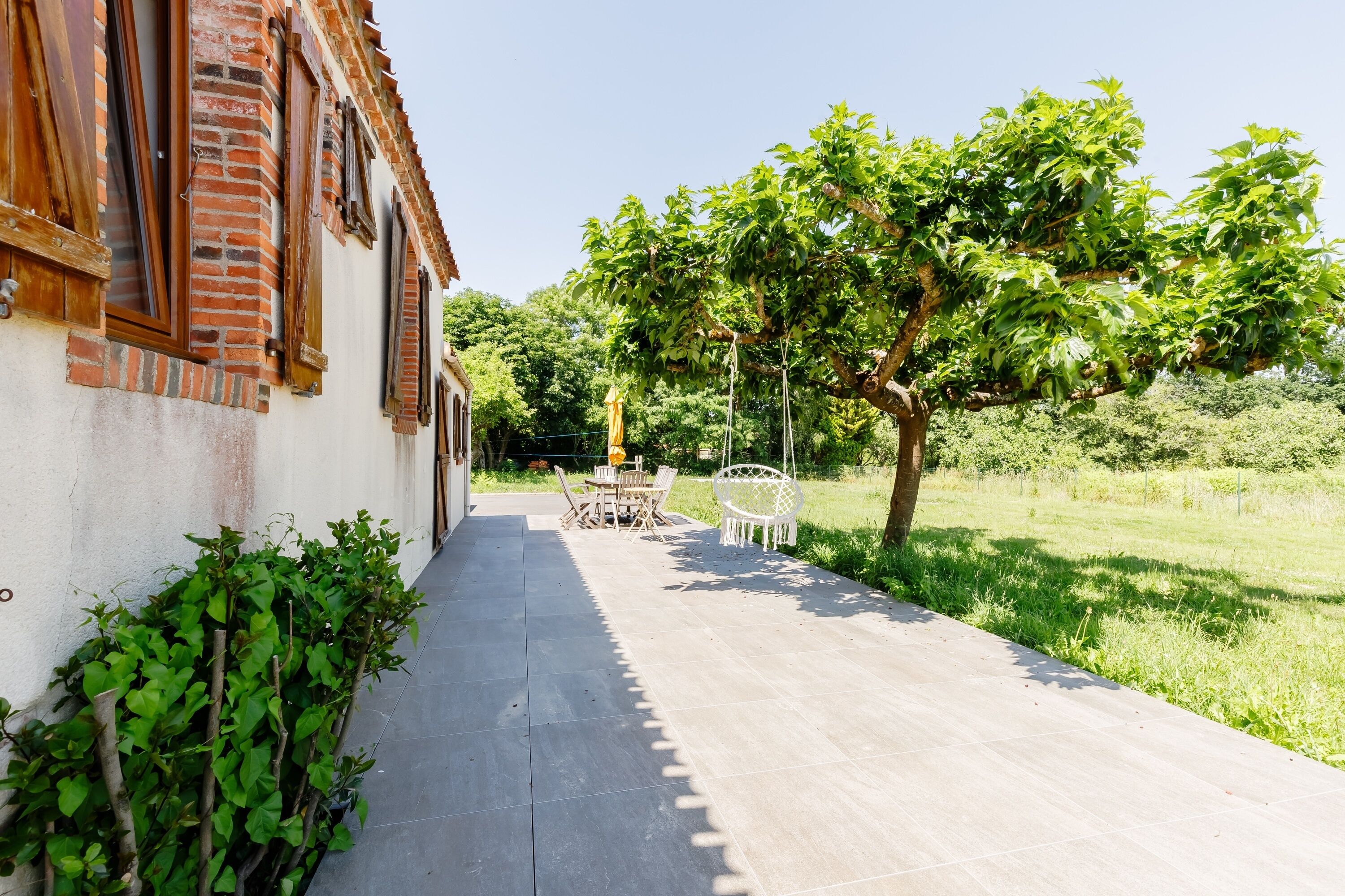 A pathway leading to a building with a brick facade and a garden area with a table and chairs.