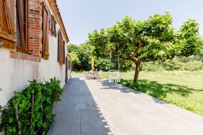 Un chemin menant à un bâtiment à la façade en briques, avec un espace jardin comprenant une table et des chaises.
