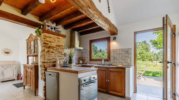 A kitchen with a stone wall, wooden cabinets, a built-in oven, and a large window. - La Chaumière de Jeannot - Maison avec jardin pour 8 (La Chapelle-Hermier)