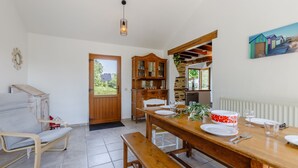 A dining area with a wooden table set for four, a bench, a wooden cabinet, and a door leading outside. - La Chaumière de Jeannot - Maison avec jardin pour 8 (La Chapelle-Hermier)