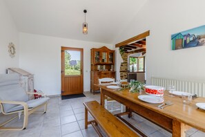 Un coin repas avec une table en bois dressée pour quatre personnes, un banc, un buffet en bois et une porte donnant sur l’extérieur.