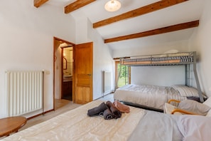 Une chambre avec un lit superposé, un plafond en bois, un radiateur et une porte donnant sur une salle de bain.