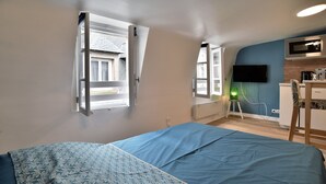 A bedroom with a bed, a desk, a chair, a TV, and a window. - Le Cocon des Remparts - Au coeur de l'intramuros (Saint-Malo)