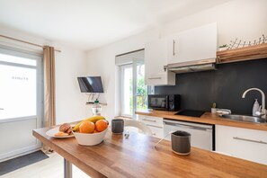 A modern kitchen with a wooden countertop, a microwave, a sink, and a television mounted on the wall. - Le Nid Choletais - Au centre-ville de Cholet (Cholet)
