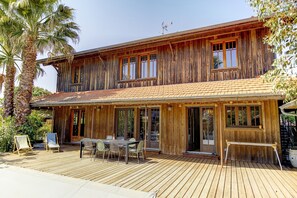 Ein zweistöckiges Holzhaus mit einer Terrasse, Sitzgelegenheiten im Freien und Palmen.