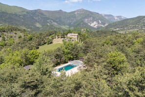 Eine Berglandschaft mit einem Schwimmbecken, einem Gebäude mit Dach und einem eingezäunten Bereich.