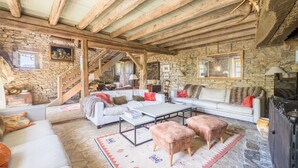 Ein rustikaler Innenraum mit Steinwänden, Holzbalken, einer Sofagarnitur, einem Couchtisch und einem Kamin.