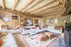 Ein rustikaler Innenraum mit Steinwänden, Holzbalken, einer Sofagarnitur, einem Couchtisch und einem Kamin.
