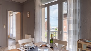 Un coin repas avec une table dressée pour deux personnes, une bouteille de vin et une vue sur la mer grâce à de grandes fenêtres.