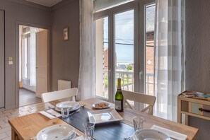 Un coin repas avec une table dressée pour deux personnes, une bouteille de vin et une vue sur la mer grâce à de grandes fenêtres.