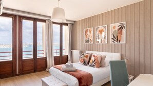 A bedroom with a large bed, wooden panel walls, a view of the sea, and a white chair. - Bel Horizon Marin - Magnifique vue mer (Saint-Malo)