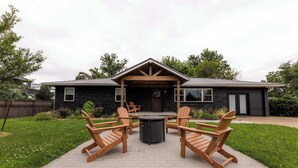 Una casa con patio amueblado con sillas tipo Adirondack y una mesa redonda.