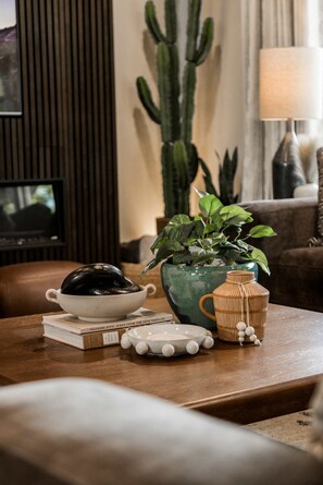 A living room with a wooden coffee table, a green plant, a white bowl, a book, and a lamp. - Enjoy the Ride | Walk to Square | Bike Friendly (Bentonville)
