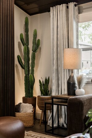 A cozy living room with a large cactus, a lamp, a wicker basket, and a cushioned chair. - Enjoy the Ride | Walk to Square | Bike Friendly (Bentonville)