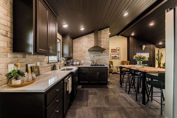 A modern kitchen with dark cabinetry, a brick backsplash, and a central island with stools. - Enjoy the Ride | Walk to Square | Bike Friendly (Bentonville)