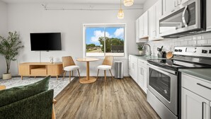 Una cocina moderna con armarios blancos, electrodomésticos de acero inoxidable, un televisor de pantalla plana y un comedor con una mesa redonda y sillas.